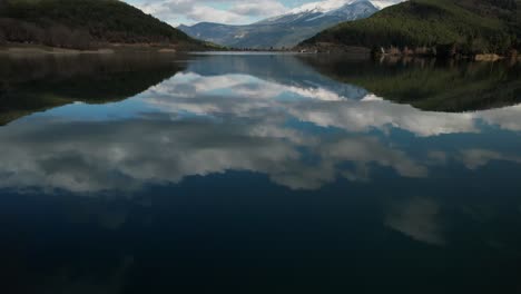 Sky-Clouds-Reflected-on-Waters-of-Lake-Doxa,-Greece-Travel-and-Tourism-Destination-between-Green-Pine-Forests-in-Cinematic-Scenic-Landscape