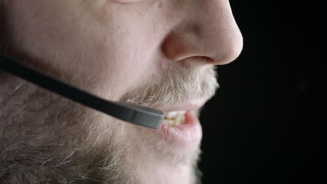 Lower-face-against-black-background,-man-speaks-into-phone-headset