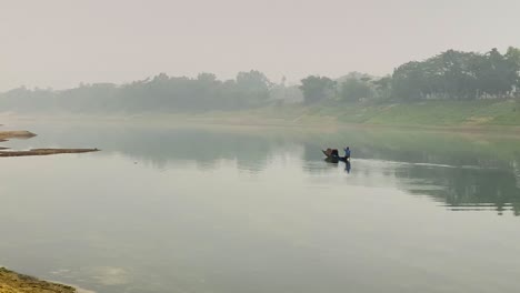 Fishermen-paddle-a-small-boat-on-a-foggy-Asian-river,-surrounded-by-serene-natural-beauty