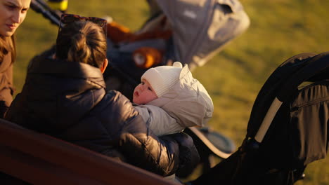 Retrato-De-Un-Bebé-En-Brazos-De-Su-Madre-En-Un-Banco-En-Un-Parque-Público-De-La-Ciudad,-En-Una-Tarde-De-Primavera