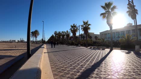 People-silhouettes-walking-on-the-boulevard-along-Malvarrosa-Beach-in-Valencia,-Spain-at-sunset