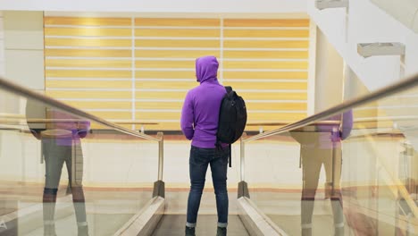 Fullshot-of-man-standing-on-inclined-moving-walkways,-wearing-purple-hoodie