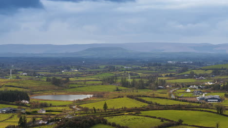 Time-lapse-of-rural-farming-landscape-with-grass-fields,-lake-and-hills-during-a-cloudy-day-viewed-from-Keash-caves-in-county-Sligo-in-Ireland