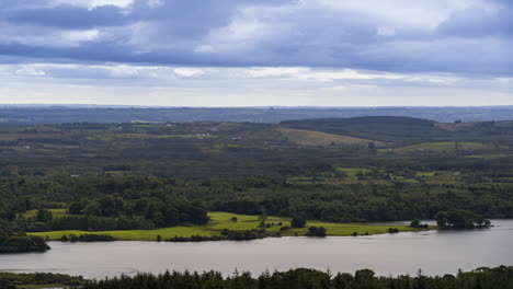 Time-lapse-of-rural-farming-landscape-with-lake,-forest-and-hills-during-a-cloudy-day-viewed-from-above-Lough-Meelagh-in-county-Roscommon-in-Ireland