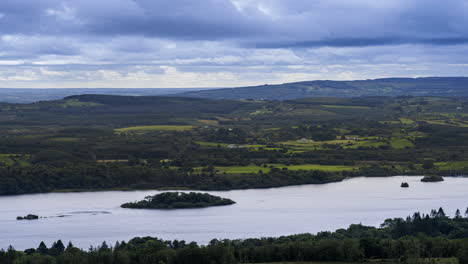 Time-lapse-of-rural-farming-landscape-with-lake,-forest-and-hills-during-a-cloudy-day-viewed-from-above-Lough-Meelagh-in-county-Roscommon-in-Ireland