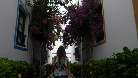 Frau-Geht-Durch-Die-Straßen-Von-Puerto-De-Mogan-Mit-Wunderschönen-Gebäuden,-Die-Mit-Wundervollen-Blumen-Geschmückt-Sind,-Und-Bei-Sonnenuntergang