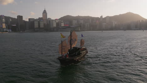 Traditionelles-Aqua-Luna-Dschunkenboot-Mit-Hongkong-Inselpanorama-Und-Victoria-Hafen-Im-Hintergrund,-Drohnenschwenkaufnahme