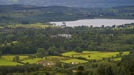 Time-lapse-of-rural-farming-landscape-with-lake,-forest-and-Kilronan-castle-during-a-cloudy-day-viewed-from-above-Lough-Meelagh-in-county-Roscommon-in-Ireland
