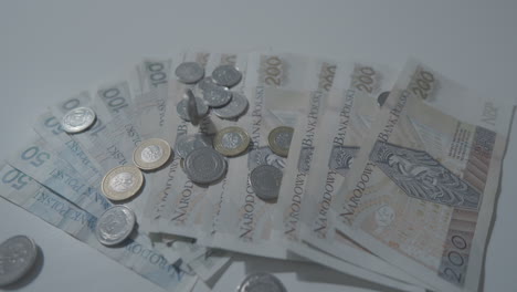 Close-up-shot-showing-falling-polish-zloty-coins-on-banknotes-on-white-table