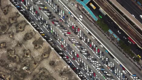 Rotating-Aerial-Shot-of-a-Congested-Car-Park,-between-a-Main-Road-covered-in-Traffic-and-an-Empty-Wasteland,-Bangkok,-Thailand