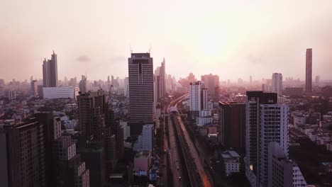 Toma-Aérea-De-Un-Amanecer-Nublado-Detrás-Del-Moderno-Paisaje-Urbano-De-Bangkok,-Tailandia