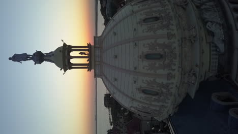 Man-stands-in-sunset-rotunda-on-ornate-building-dome-as-evening-sets