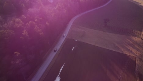 Drone-Shot-following-tow-Cars-on-a-Forest-Road-during-Sunset