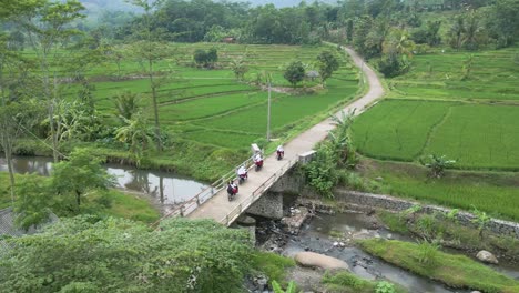 Travellers-on-bikes-crossing-a-bridge,-driving-through-rural-Indonesia,-rice-fields-left-and-right