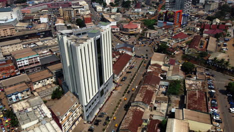 Aerial-view-of-traffic-in-front-of-the-Hotel-Adamaoua,-in-sunny-Yaounde,-Cameroon---pan,-drone-shot