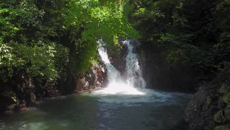 Young-man-swims-in-pool-below-dense-jungle-waterfall-in-Bali