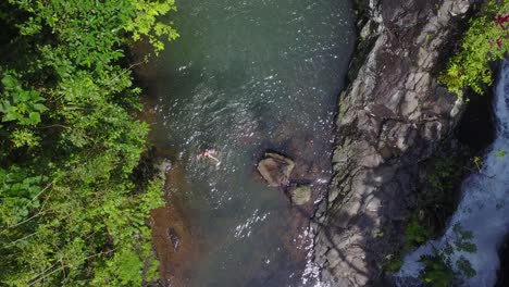 Rising-aerial:-Tourist-woman-enjoys-splashing-in-jungle-waterfall-pool