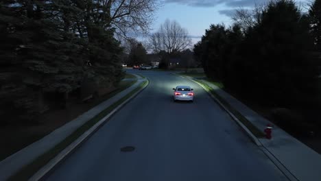 White-sedan-driving-through-residential-neighborhood-in-America-at-night
