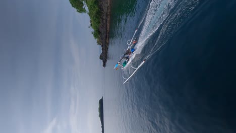 Vertical-FPV-Drone-shot-of-traditional-Indonesian-boat-sailing-over-a-calm-sea-on-a-sunny-day