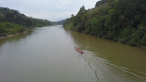 Tracking-Luftaufnahme-Eines-Bootsmanns,-Der-Ein-Leeres-Boot-Den-Jungle-River-In-Laos-Hinauffährt