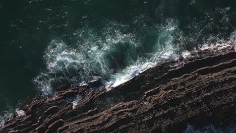 Ocean-waves-and-rocky-reefs-or-cliffs,-drone-aerial-top-down-ascending-view