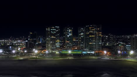 Aerial-dolly-left-shot-of-bright-lights-on-in-the-beachfront-skyscrapers-in-Iquique,-Chile