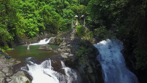 Female-Caucasian-tourist-splashes-water-in-jungle-waterfall-pool,-Bali