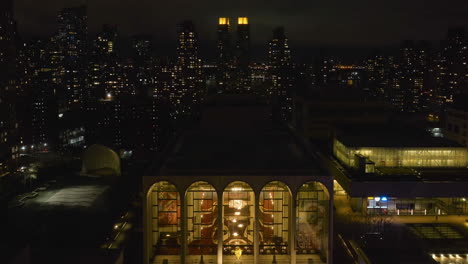 Vista-Aérea-Frente-Al-Centro-Iluminado-De-Lincoln-Para-Las-Artes-Escénicas,-Noche-En-Nueva-York,-Estados-Unidos---Ascendente,-Disparo-De-Drones