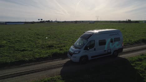 Aerial-view-tracking-campervan-travelling-on-journey-on-green-rural-agricultural-road