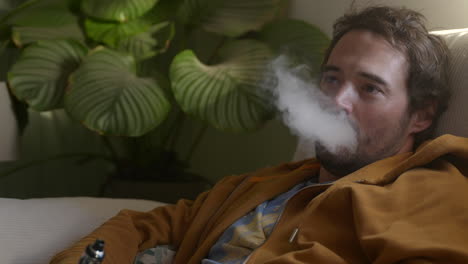 Hombre-Guapo-Fumando-Cigarrillo-Electrónico-En-El-Sofá-De-Casa,-Vista-De-Cerca