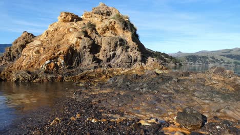 Sea-water-gently-laps-beside-trachyte-and-basalt-volcanic-rock-formations---Onawe-Peninsula,-Akaroa-Harbor