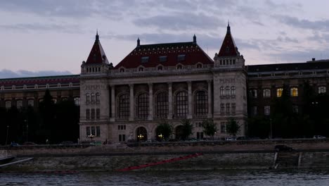Close-up-hand-held-shot-of-Budapest-University-of-Technology-and-Economics-building-at-golden-hour,-shot-from-the-Danube-River-in-Budapest,-Hungary