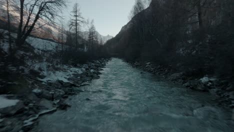 Fast-dolly-over-cold-Swiss-flowing-river-water-stream-with-snow-on-river-banks-in-Switzerland-Alps-with-epic-mountain-panorama