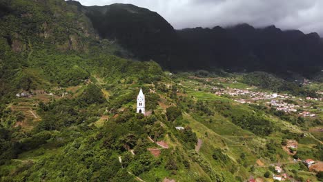 Aerial-view-of-chapel-on-top-of-green-hill-in-a-mountain-valley-landscape,-Sao-Vicente,-Madeira
