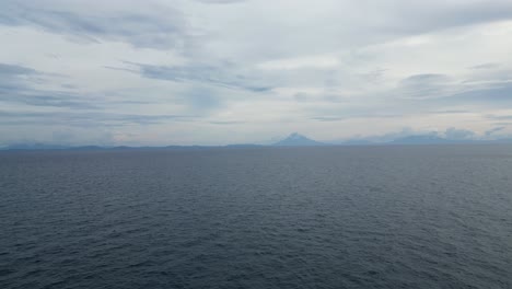 Entspannende-Luftaufnahme-Des-Unberührten,-Plätschernden-Meerwassers-Und-Der-Atemberaubenden-Wolkenlandschaft-Mit-Der-Silhouette-Des-Mayon-Vulkans-Im-Hintergrund