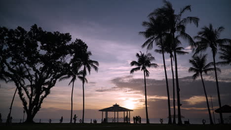 Tanjung-Aru-Beach---Silhouetted-Tropical-Palms-and-People-Tourists-Walking-Against-Dramatic-Sunset-Sky-by-the-Sea-at-Shangri-la-Resort-Kota-Kinabalu,-Sabah,-Malaysia---static-wide-angle