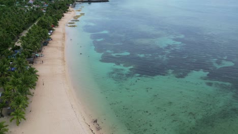Stunning-Aerial-View-of-idyllic,-white-sand-beach-with-crystal-clear-waters,-bangka-boats,-and-shallow-reef-in-the-island-of-Catanduanes