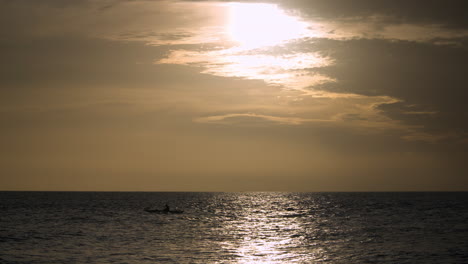 Silhouetted-man-on-a-kayak-floats-in-the-reflection-of-the-sunset-on-the-water