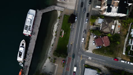 aerial-top-down-of-Queenstown,-New-Zealand-drone-fly-above-busy-traffic-street-and-coastline-with-sail-boat-moored-at-dock