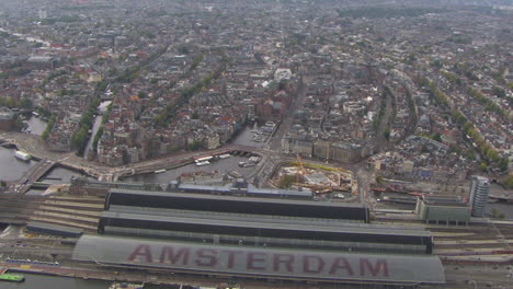 Toma-Aérea-De-Establecimiento-De-La-Estación-Central-De-Amsterdam-Con-El-Centro-De-La-Ciudad-Detrás