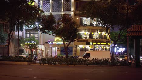 Actividad-De-Tráfico-Con-Tiendas-En-El-Fondo-Capturada-Desde-Un-Parque-Por-La-Noche-En-La-Ciudad-De-Ho-Chi-Minh,-Vietnam