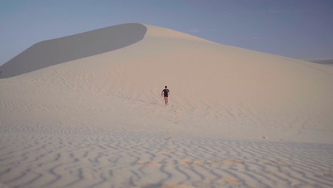 Man-wearing-black-running-down-the-White-Sand-Dunes-in-Mui-Ne,-Phan-Thiet,-Vietnam