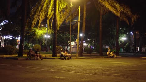 Park-goers-sitting-on-the-bench-chilling-and-playing-da-cau-in-a-park-at-night-in-District-1-Ho-Chi-Minh-City,-Vietnam