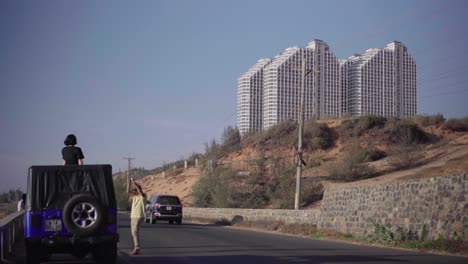 Actividad-De-Tráfico-Y-Turistas-En-Una-Carretera-Costera-A-Lo-Largo-Del-Mar-Del-Sur-De-China-Con-Un-Edificio-Alto-En-El-Fondo-En-Mui-Ne,-Phan-Thiet,-Vietnam