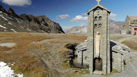 Drone-passing-near-bell-tower-of-small-stone-church,-Col-de-l'Iseran-mountain-pass,-France