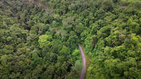 Aerial-view-of-remote-curvy-road-with-motorcyclists-over-top-of-mountain-with-green-jungle-in-Sumbawa-Island,-Indonesia