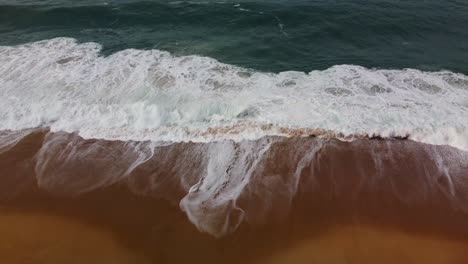 Aerial-View-Of-Nazare-Beach-Waves-Breaking-With-White-Foam-Along-Coastline