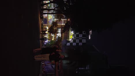 Parkgoers-strolling-in-a-park-at-night-with-neon-lights-in-the-background-in-Ho-Chi-Minh-City,-Vietnam-vertical