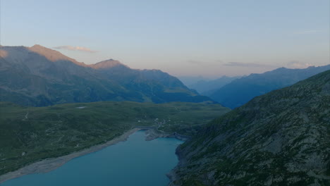 Aerial-shot-over-a-lake-with-mountains-on-the-horizon-at-sunset-in-montespluga,-Lombardy