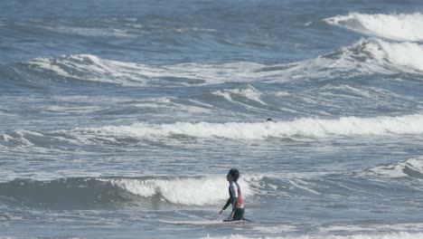 Beginner-surfer-trying-to-surf-in-shallow-water,-walking-against-small-waves
